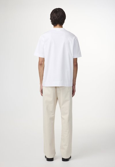 Witte katoenen t-shirt met korte mouwen, ronde halslijn en een rechte pasvorm, gecombineerd met lichtbeige, relaxed-fit broeken en zwarte schoenen.