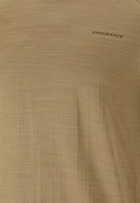 Kortærmet T-shirt med rund hals i en afdæmpet guldfarve, lavet af et struktureret stof. Har sort "ENDURANCE" logo på den øverste venstre side.