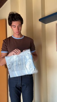 Mees hoiab plastikkattes pakki, millel on helesinine silt, seljas pruun särgiga, millel on helesinine äär ja tummad teksad.