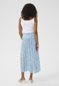 Jupe midi florale bleu clair avec des motifs verts et blancs, taille élastique, assortie à un débardeur blanc et des sandales à talons carrés blanches.
