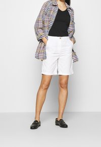 Blazer a quadri con motivo multicolore, top nero a V, pantaloni corti bianchi arrotolati e mocassini neri, caratterizzati da un dettaglio con bottone sui pantaloni.