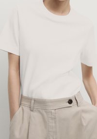 Hvid kortærmet T-shirt med rund halsudskæring, parret med lyse beige højtaljesbukser med knapdetalje og forlommer.