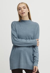 Un pull en tricot bleu clair à manches longues avec un col montant. Dispose d'une coupe décontractée et de poignets côtelés, fabriqué dans un tissu doux.