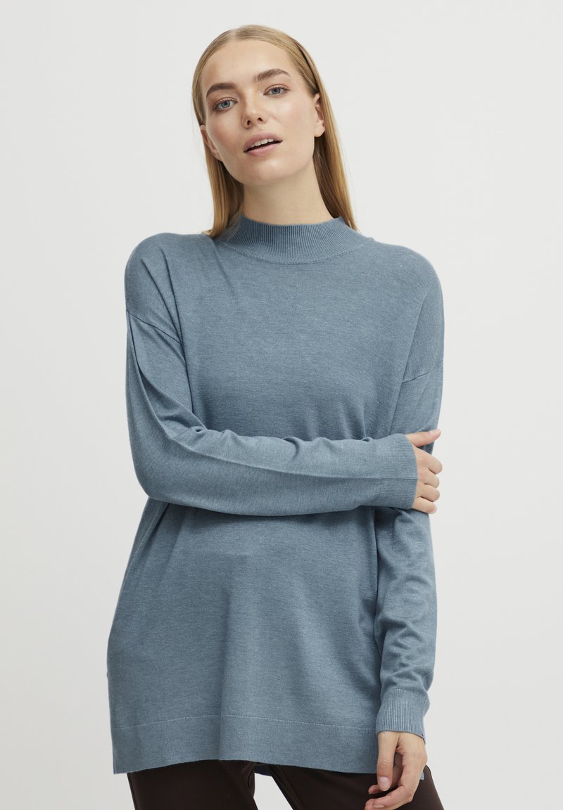 Un pull en tricot bleu clair à manches longues avec un col montant. Dispose d'une coupe décontractée et de poignets côtelés, fabriqué dans un tissu doux.