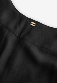 Black textile close-up featuring a smooth texture with a subtle sheen, accented by a small, golden logo button on the neckline.