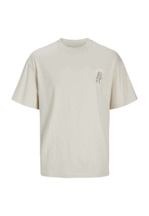 Camiseta de algodón beige con mangas cortas y cuello redondo. Presenta un pequeño gráfico floral en azul y púrpura en el área del lado izquierdo del pecho.