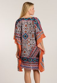 Värikäs kaftan, jossa on musta, valkoinen, turkoosi, oranssi ja punainen geometrinen kuvio, sekä virtaava muotoilu ja leveät hihat.