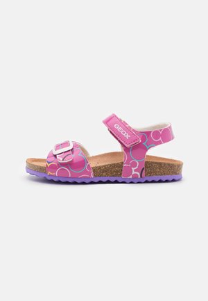 Sandalias rosas con patrones circulares, plantilla de corcho, correa ajustable y suela de goma morada. Logo de la marca visible en la correa.