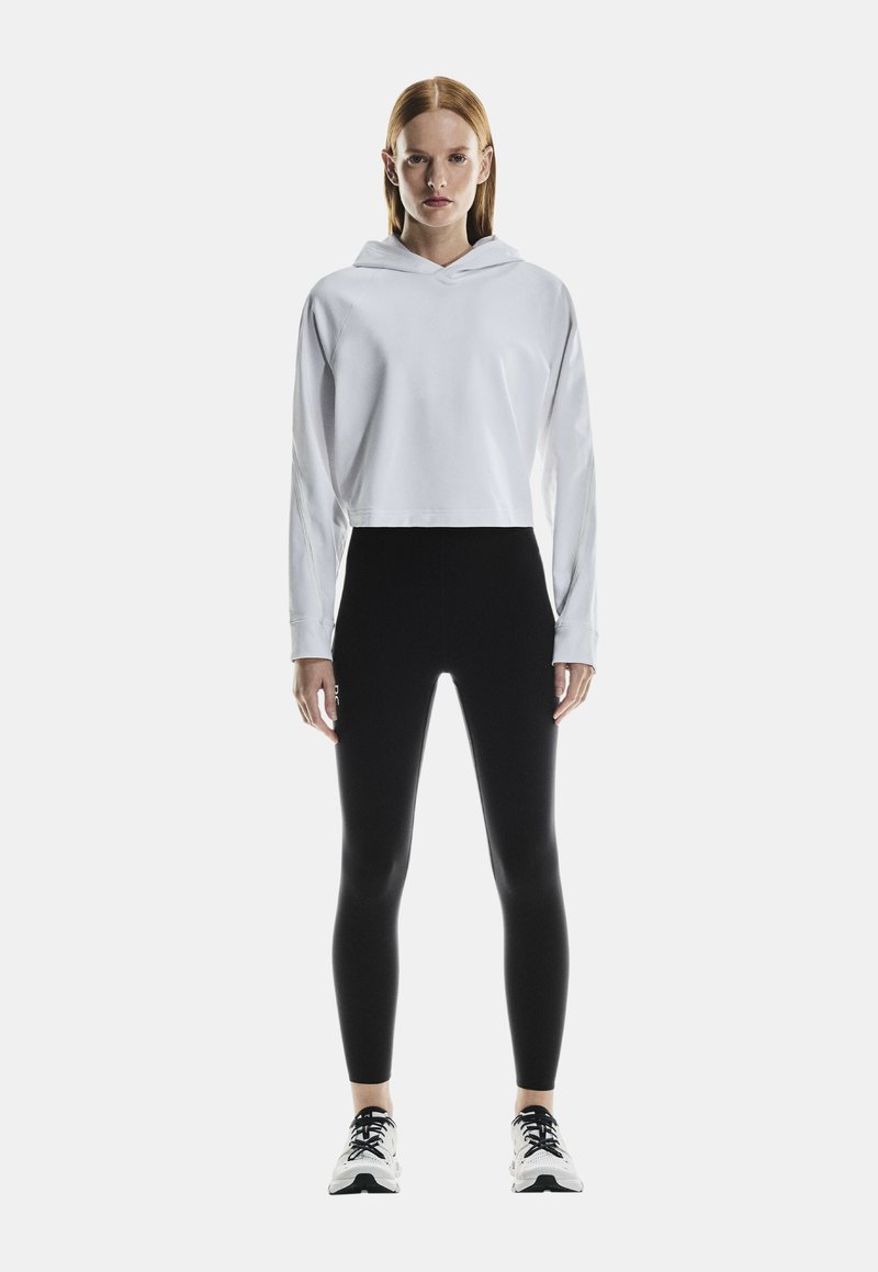 Fehér cropped kapucnis pulóver, magas derekú fekete leggingsszel párosítva. A szettet fekete-fehér sportcipők egészítik ki.