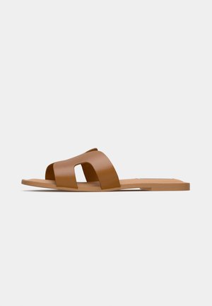 Bruna platta sandaler med breda korsade remmar av slätt syntetmaterial och en platt, minimalistisk sula.