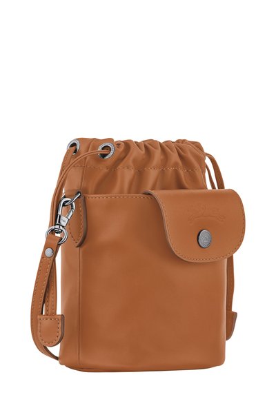 Tan leather drawstring bag with a metallic snap closure, adjustable strap, and gathered top. Features silver-tone hardware and smooth texture.