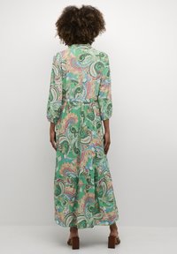 Maksi obleka v zeleni paisley vzorec, dolgi rokavi, zategnjen pas, tekoča krila, z večplastnimi ruffles na robu in mehkim tekstilom.