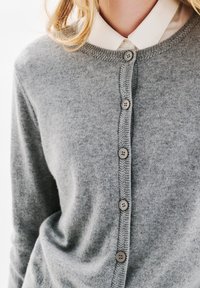 Cardigan grigio realizzato in morbido tessuto a maglia, con scollatura rotonda, chiusura a bottoni frontale con cinque bottoni grigi e una banda testurizzata lungo il bordo.
