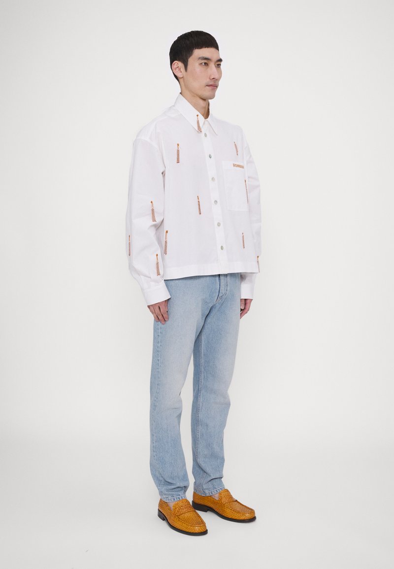 Hvid skjorte med orange dekorative detaljer, brystlomme, knaplukning; parret med lyseblå jeans og orange vævede sko.