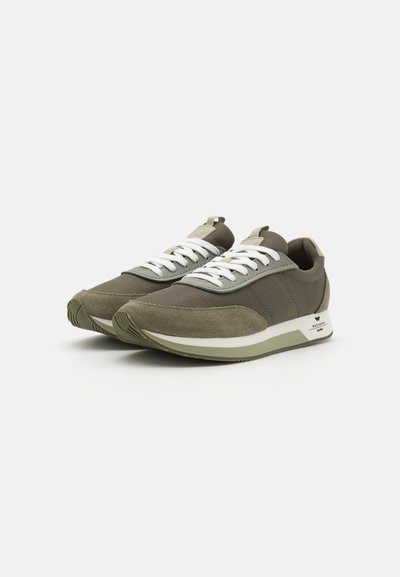 Leichte Sportschuhe in Olivgrün mit Mesh- und Wildlederpaneelen, weißen Schnürsenkeln und einer strukturierten Gummisohle. Das Design umfasst eine Ziehlasche.