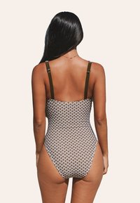 El traje de baño de una pieza presenta un patrón geométrico marrón con acentos en blanco, tirantes delgados ajustables y un diseño de pierna alta.
