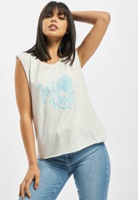 Lys grå ermeløs topp med en spraglete tekstur og blå trykt tekst, med et bladgrafikk, kombinert med blå jeans.