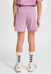 Lila sportshorts met elastische tailleband, gecombineerd met witte sokken met een zwart chevron-patroon en witte sneakers met logo.