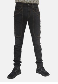 Jeans in denim scuro con una vestibilità slim, caratterizzati da cuciture a contrasto, tasche frontali e una piccola patch con logo. Abbinati a sneakers nere.