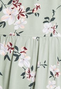 Klänning med blommönster i ljusgrönt tyg, prydd med vita, rosa och mörkröda blommor. Innsvängt i midjan med mjuk textur.