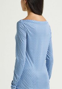 Haut bleu à manches longues présentant un motif géométrique texturé. Tissu lisse avec un col large et une silhouette ajustée.