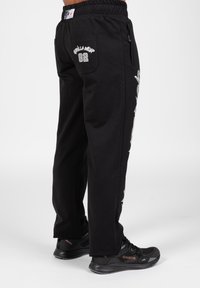 Zwarte trainingsbroek met een elastische tailleband, zijzakken met rits en witte grafische prints aan de zijkanten, met "Gorilla Wear 82" op de achterzak.