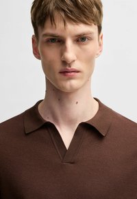 Brun texturerad pikétröja med V-ringning och korta ärmar, med krage och ett subtilt vävt mönster.