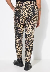 Pantalones de leopardo en beige, con manchas negras y rosas. Corte ajustado con bolsillos, combinados con botas de plataforma negras con tachuelas.