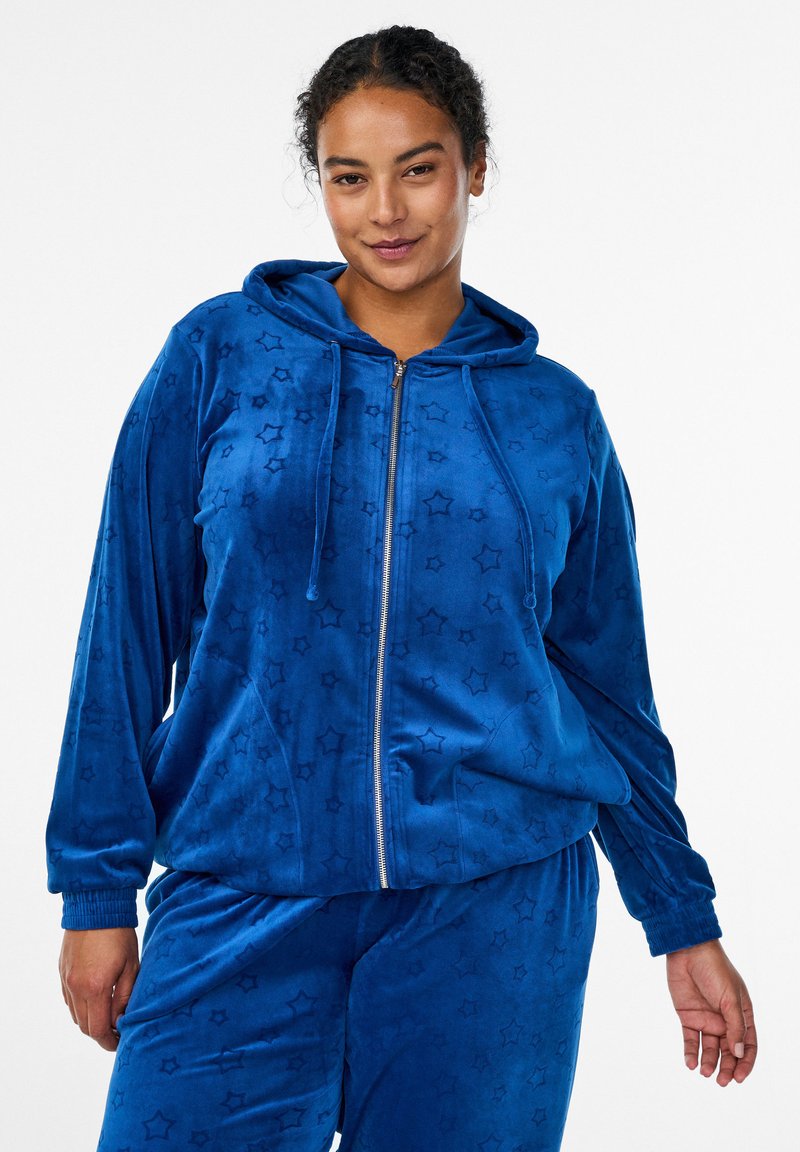 Blauer Velours-Trainingsanzug mit einer Kapuzenjacke mit Reißverschluss und passenden Hosen, geprägtem Sternenmuster, elastischen Bündchen und entspannter Passform.