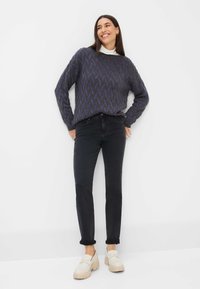 Overmaat, gebreide trui in donkergrijs met een zigzagpatroon in paars, gecombineerd met zwarte jeans en beige platformloafers.