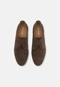 Braune Wildlederschuhe mit einer abgerundeten Zehenpartie, die ein Schnürdesign und gestickte Akzente im Obermaterial aufweisen. Weiche Textur; minimalistische Stil.