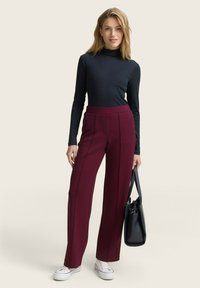 Bordeaux wijde broek met voorplooien, gecombineerd met een aansluitend zwart langemouwen shirt en witte sneakers. Zwarte handtas inbegrepen.