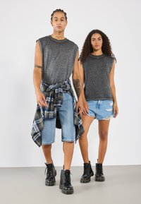 Grå melange ermeløse topper, lyseblå slitte shorts, og rutete skjorte knyttet i livet; begge har på seg svarte snørestøvler.