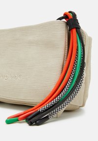 Beige farbige Tasche mit mehreren Reißverschlussanhängern in Orange, Grün, Schwarz mit Muster und Rot. Markenlogo auf der Seite geprägt.