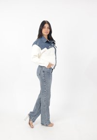 Jeansjacka med vit stickad kropp och blå denimärmar, med knäppning fram och två bröstfickor; matchad med ljusblå jeans.