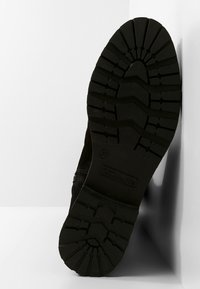 Musta jalkineen pohja, jossa on syvä pinta kuvio, joka tarjoaa pitovoimaa. Se on valmistettu kumista, jossa on karheapintainen pinta ja selkeä kanta.