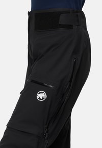 Zwarte outdoor broeken met een gladde textuur, ritszakken en een logo-opdruk. De tailleband heeft een klittenbandsluiting voor aanpassingsmogelijkheden.