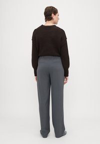 Brauner Strickpullover mit überschnittenen Schultern, kombiniert mit grauen weiten Hosen. Die Hose verfügt über einen Kordelzugbund und hintere Taschen.
