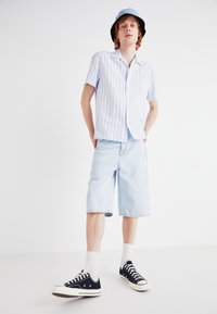 Short-sleeve button-up shirt in light blue with white stripes, paired with light blue denim shorts and black sneakers with white soles.
