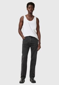 Hvid ærmeløs top og sorte lige ben jeans. Toppen har en rund halsudskæring; jeansene har en falmet tekstur og fem-lomme design.