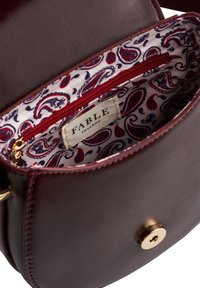 Brown leather handbag with paisley fabric lining, red zipper pocket, and gold magnetic clasp, showing FABLE England brand label inside.
