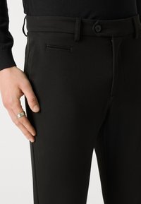 Black trousers with a smooth texture, featuring a narrow fit, side pocket, and button closure at the waist.