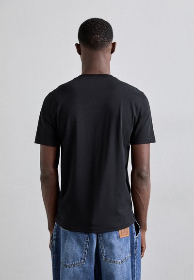 T-shirt nera in cotone con maniche corte, caratterizzata da un collo rotondo, texture liscia e una vestibilità comoda. Vista da dietro con cuciture visibili.