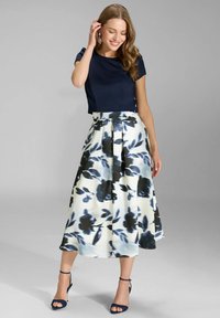 Marineblaues Kurzarmoberteil kombiniert mit einem knielangen Rock mit Blumenmuster in Weiß- und Blautönen. Das Modell trägt blaue Riemchenabsätze.