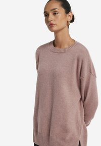 Rosa oversized Pullover mit Rundhalsausschnitt, geripptem Saum und überschnittenen Schultern, aus weichem Material mit glatter Textur gefertigt.