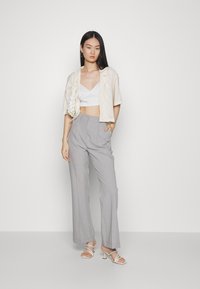 Camisa curta de botão em cor clara, top bustier branco, calças largas cinzentas e sandálias de salto alto com tiras. Os acessórios incluem uma bolsa texturizada.