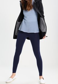 Leggings azul marino combinados con una parte superior de rayas azul claro y una chaqueta con capucha negra, que presenta bolsillos interiores grises y un diseño de dobladillo acampanado.