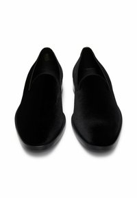 Scarpe nere senza lacci con una texture in tessuto liscia, forma allungata e design minimalista. Suole in gomma e nessun hardware o accenti visibili.