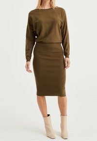 Top en tricot vert olive à manches longues associé à une jupe midi côtelée ajustée. La tenue présente un design simple et une texture lisse.