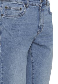 Jeans de denim azul claro con una textura ligeramente descolorida, que presentan un bolsillo frontal, costuras cosidas y detalles de botones metálicos.